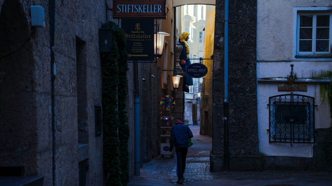 A single anonymous figure walking down a quiet European street at dusk